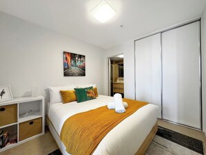 Cozy retreat with a neatly made bed, framed picture, and a few books on a bedside shelf.