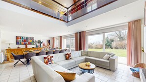 A spacious living room with a large sectional sofa, a dining area with a wooden table and chairs, and a view of the outdoors through large windows. - 7 bedroom beautiful home in Flaignes-Havys (Flaignes-Havys)