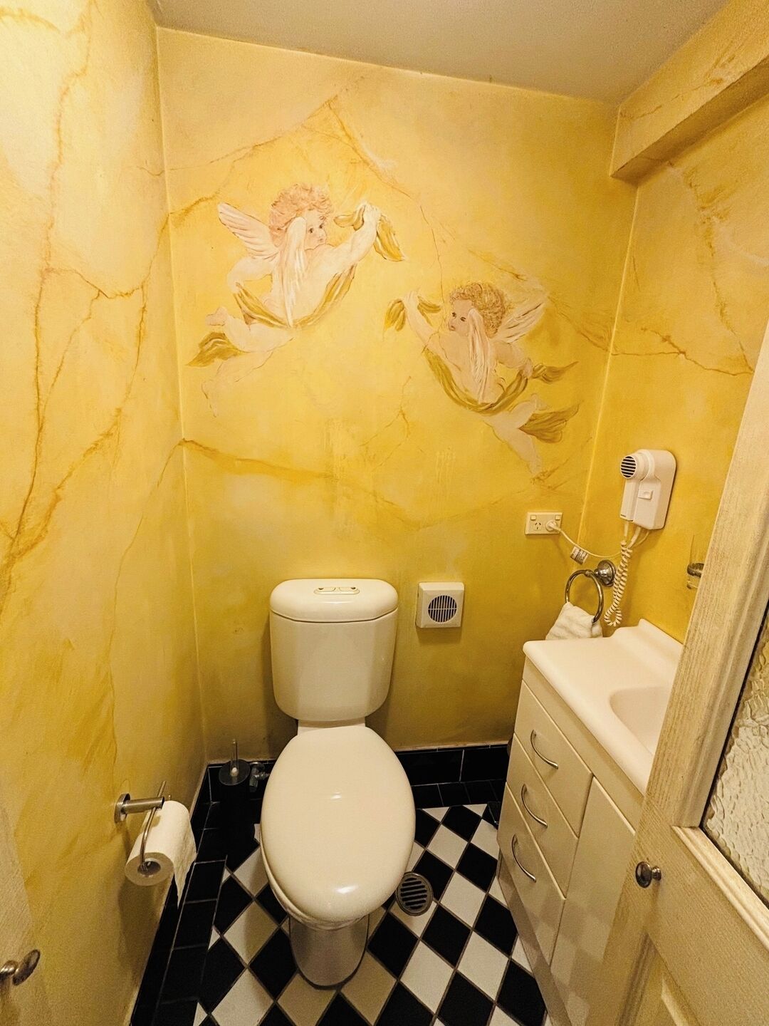 A bathroom with a toilet, sink, and a decorative mural on the wall.