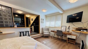 A modern hotel room with a large bed, a desk, a chair, a TV, and a staircase leading to a kitchen. - Leura's Magical Manderley - Studio Room (Leura)