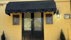 A yellow building with a black awning, a black door, and two decorative windows. - Leura's Magical Manderley - Studio Room (Leura)