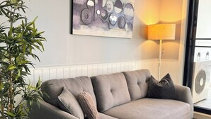 A grey sofa with multiple cushions, a bamboo plant, a wall-mounted abstract painting, and a standing floor lamp. - Central Parramatta 2BR | Steps from Train and Shops (Parramatta)