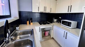 A modern kitchen with white cabinets, a stainless steel sink, a stove, an oven, and a microwave. - Central Parramatta 2BR | Steps from Train and Shops (Parramatta)