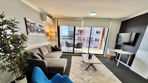 A modern living room with a sofa, a blue chair, a small table, and a TV. - Central Parramatta 2BR | Steps from Train and Shops (Parramatta)
