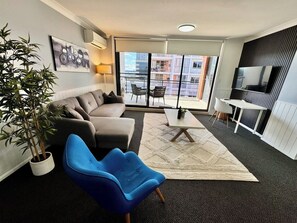 Ein modernes Wohnzimmer mit einer Couch, einem blauen Sessel, einem kleinen Tisch und einem Fernseher.