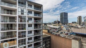 A multi-story residential building with balconies, a parking lot, and a modern high-rise building in the background. - Central Parramatta 2BR | Steps from Train and Shops (Parramatta)