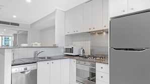 Ett modernt kök med vita skåp, vitvaror i rostfritt stål, en mikrovågsugn, en vattenkokare och en diskmaskin.