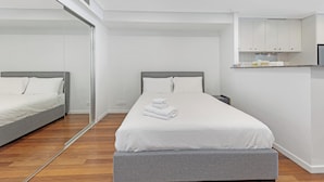 Ett modernt hotellrum med en stor säng, ett sängbord, en spegel och ett litet pentry.