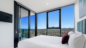 A bedroom with a large bed, a view of a cityscape through floor-to-ceiling windows, and a modern design.