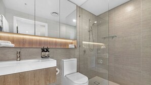 A modern bathroom with a glass-enclosed shower, a white toilet, and a wooden vanity with a mirror.