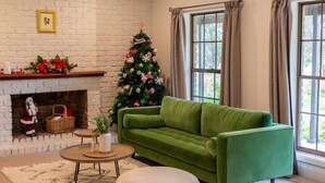A living room with a green sofa, a fireplace, a Christmas tree, and a large window.