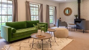 A living room with a green sofa, two round coffee tables, a beige ottoman, and a fireplace.