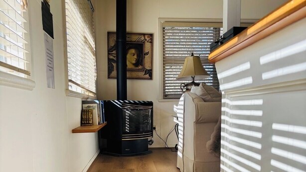 Un couloir étroit avec un plancher en bois, un radiateur noir et une fenêtre équipée de stores.