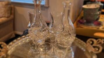 A glass tray with crystal decanters and glasses on a table in a room with a window and a sofa in the background.