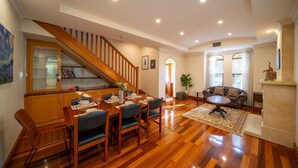 Ein Essbereich mit einem Holztisch, gedeckt für vier Personen, eine Treppe und ein Wohnzimmer mit Sofa und Kamin.