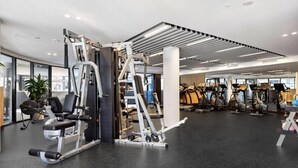 Une salle de sport moderne dotée de divers appareils d’exercice, de grandes fenêtres et d’un intérieur propre et bien éclairé.