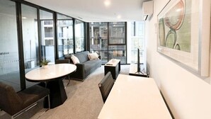 Un salon moderne et bien éclairé, comprenant un canapé, une table basse et un banc. De grandes fenêtres offrent une vue sur le paysage urbain.