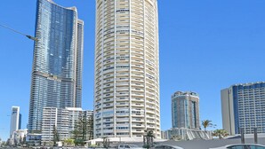 A modern high-rise building with a curved facade, multiple balconies, and a clear blue sky in the background. - Breathtaking Ocean view 3Bedrooms Unit next Beach (Surfers Paradise)