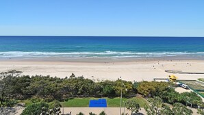 A beach with a clear blue sky, a sandy shore, and a few people. There is a lifeguard tower and a blue structure on the beach. - Breathtaking Ocean view 3Bedrooms Unit next Beach (Surfers Paradise)
