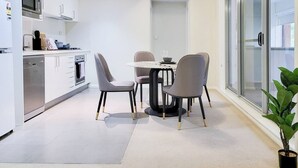 Una cocina moderna con armarios blancos, microondas integrado y lavavajillas. Hay un comedor con una mesa redonda y cuatro sillas.
