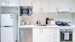 Una cocina moderna con armarios blancos, microondas integrado, lavavajillas, estufa y pileta.