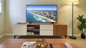 Televisor de pantalla plana sobre un mueble de madera, mostrando una vista urbana, una lámpara y una planta.