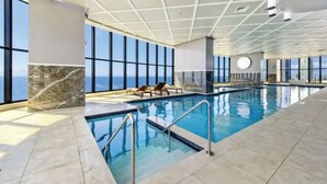Ein Innenpool mit freiem Blick auf den Ozean durch große Fenster, einer Marmorwand und einem gefliesten Boden.