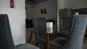 A modern dining area with a glass table and cushioned chairs, a ceiling fan, and a fire extinguisher on the wall.