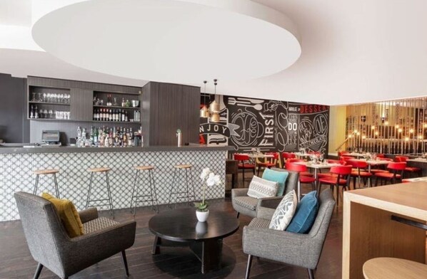 Ein moderner Barbereich mit einer Theke, Barhocker und einer Lounge mit runden Tischen und Stühlen.