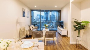 Un salon moderne avec un coin repas, de grandes fenêtres donnant sur la ville, un canapé, un téléviseur et une plante en pot.
