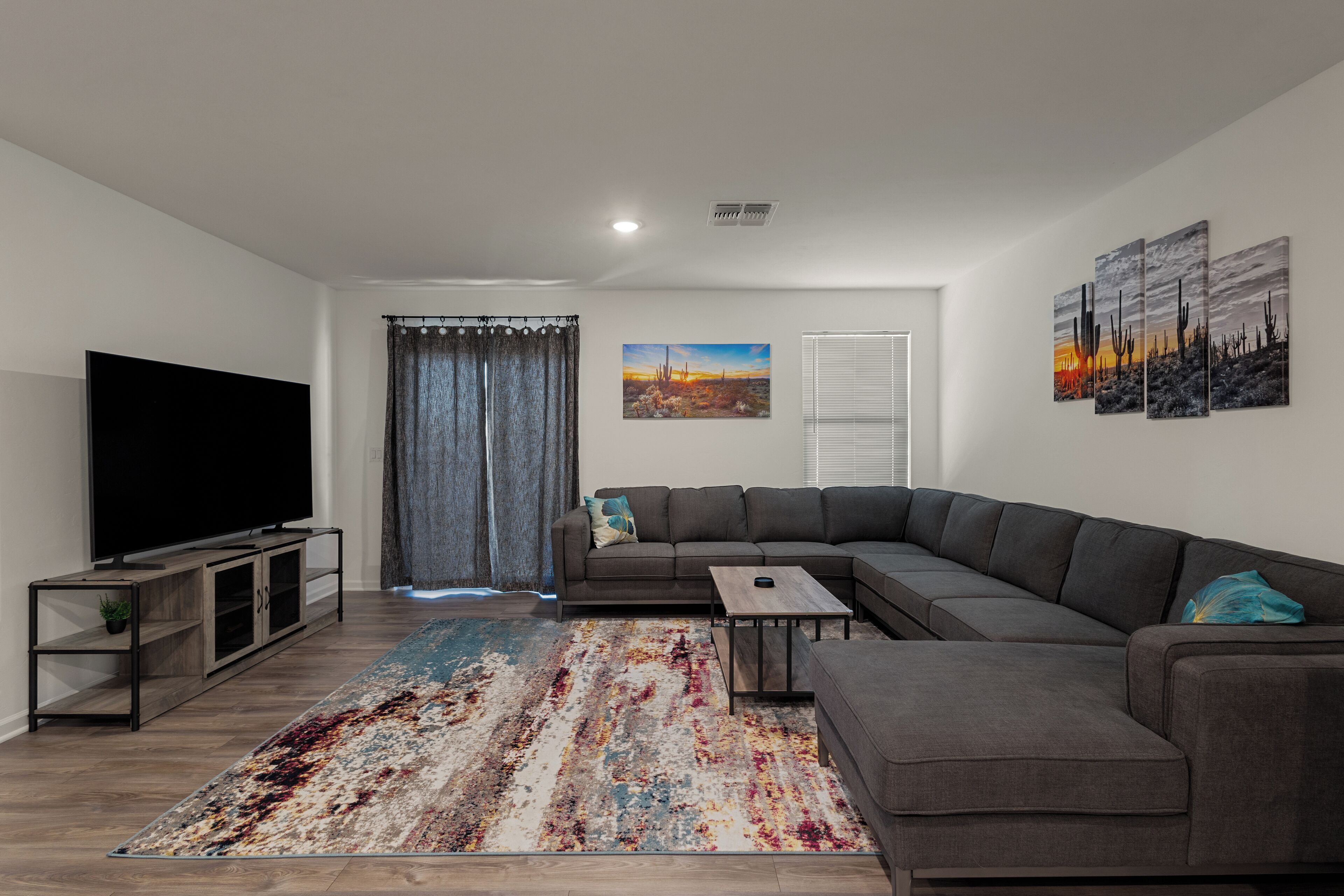A modern living room with a sectional sofa, a flat-screen TV, a coffee table, and a patterned rug.