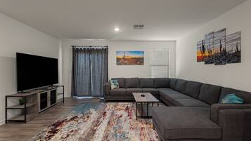 A modern living room with a sectional sofa, a flat-screen TV, a coffee table, and a patterned rug.