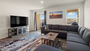 Ein modernes Wohnzimmer mit Flachbildfernseher, grauem Sofa, Couchtisch und einem gemusterten Teppich.