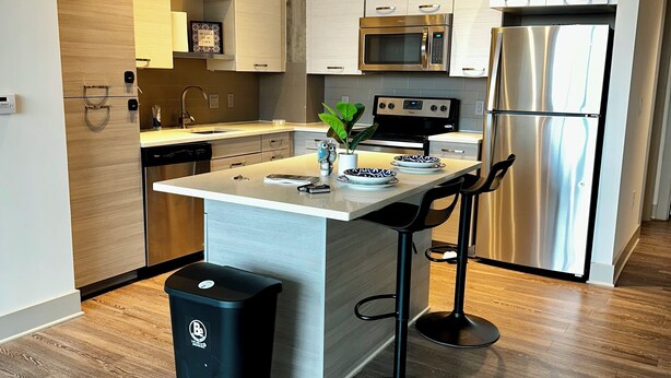 A modern kitchen with a central island, stainless steel appliances, and a black trash bin. - Cozy 1-bedroom apartment in beautiful downtown Atlanta with amazing view  (Atlanta)