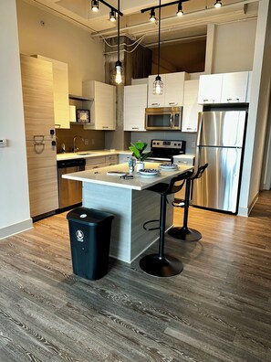 A modern kitchen with a central island, stainless steel appliances, and a black trash bin. - Cozy 1-bedroom apartment in beautiful downtown Atlanta with amazing view  (Atlanta)