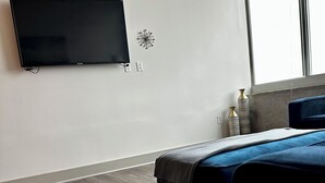A modern hotel room with a flat-screen TV mounted on the wall, a bed with a blue headboard, a marble-patterned rug, and a remote control on the floor. - Cozy 1-bedroom apartment in beautiful downtown Atlanta with amazing view  (Atlanta)