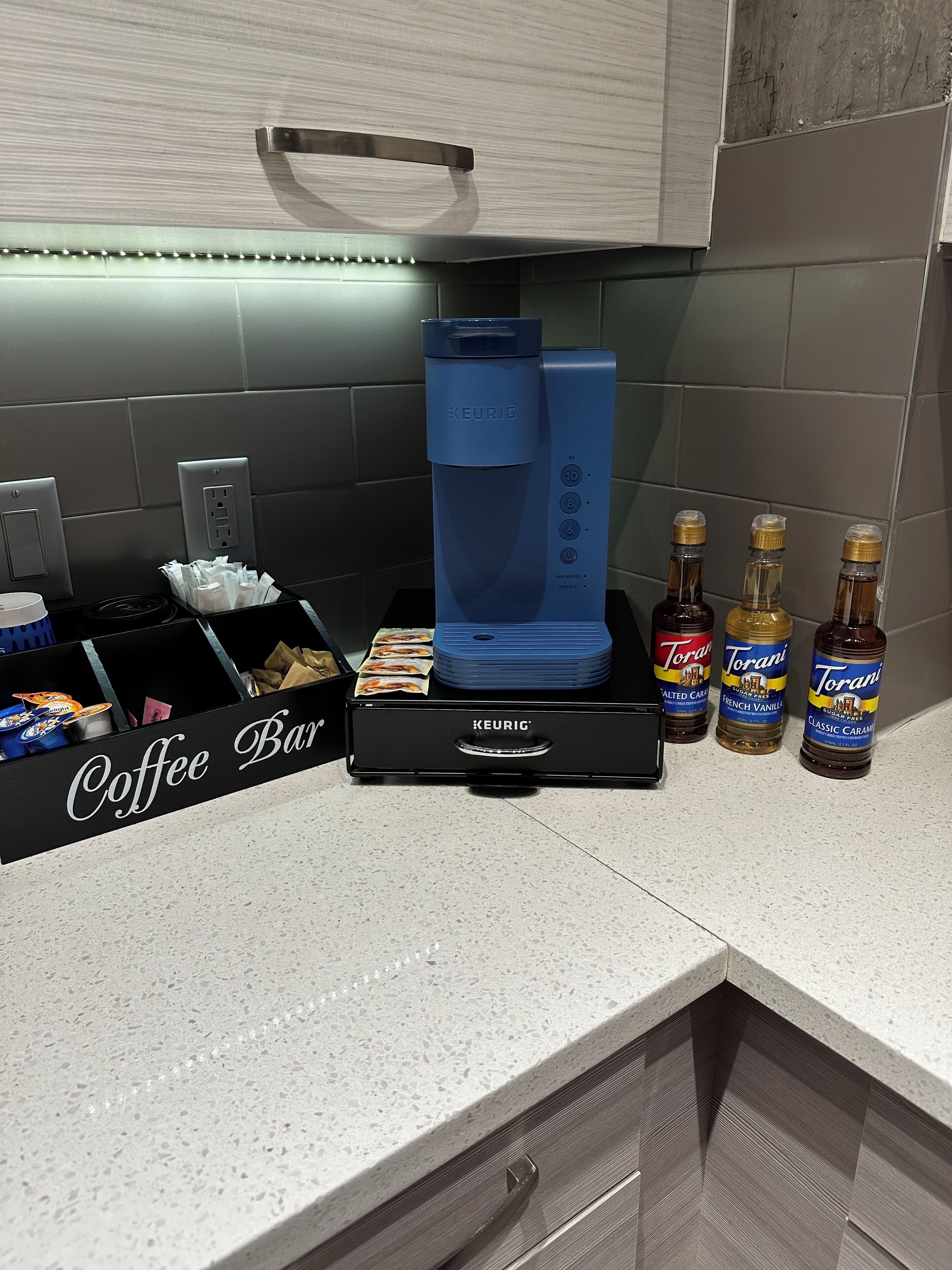 A coffee bar with a Keurig coffee maker, Torani syrups, and a coffee pod holder.