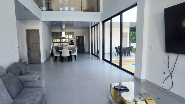 A modern living room with a grey sofa, a glass coffee table, and a TV mounted on the wall. - Thomas' Ranch (Nilo)