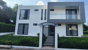 A modern two-story house with a flat roof, large windows, and a black gate. - Thomas' Ranch (Nilo)