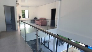 A modern interior with a glass railing, a pink sofa, and a view of the outdoors. - Thomas' Ranch (Nilo)