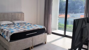 A bedroom with a bed, a window with curtains, and a view of buildings outside. - Thomas' Ranch (Nilo)