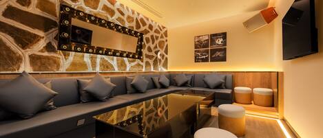 A modern living room with a stone wall, a sofa with cushions, a glass coffee table, and wooden ottomans.