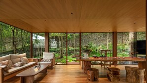 A modern living room with a wooden ceiling, large windows, a sofa, a coffee table, and a dining table with chairs. - YAOJIA WATERFALL VILLAGE RESORT (Anshun)