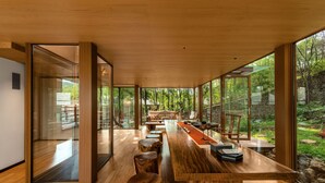 A modern interior with a wooden ceiling, large windows, a long dining table, and a stone wall. - YAOJIA WATERFALL VILLAGE RESORT (Anshun)