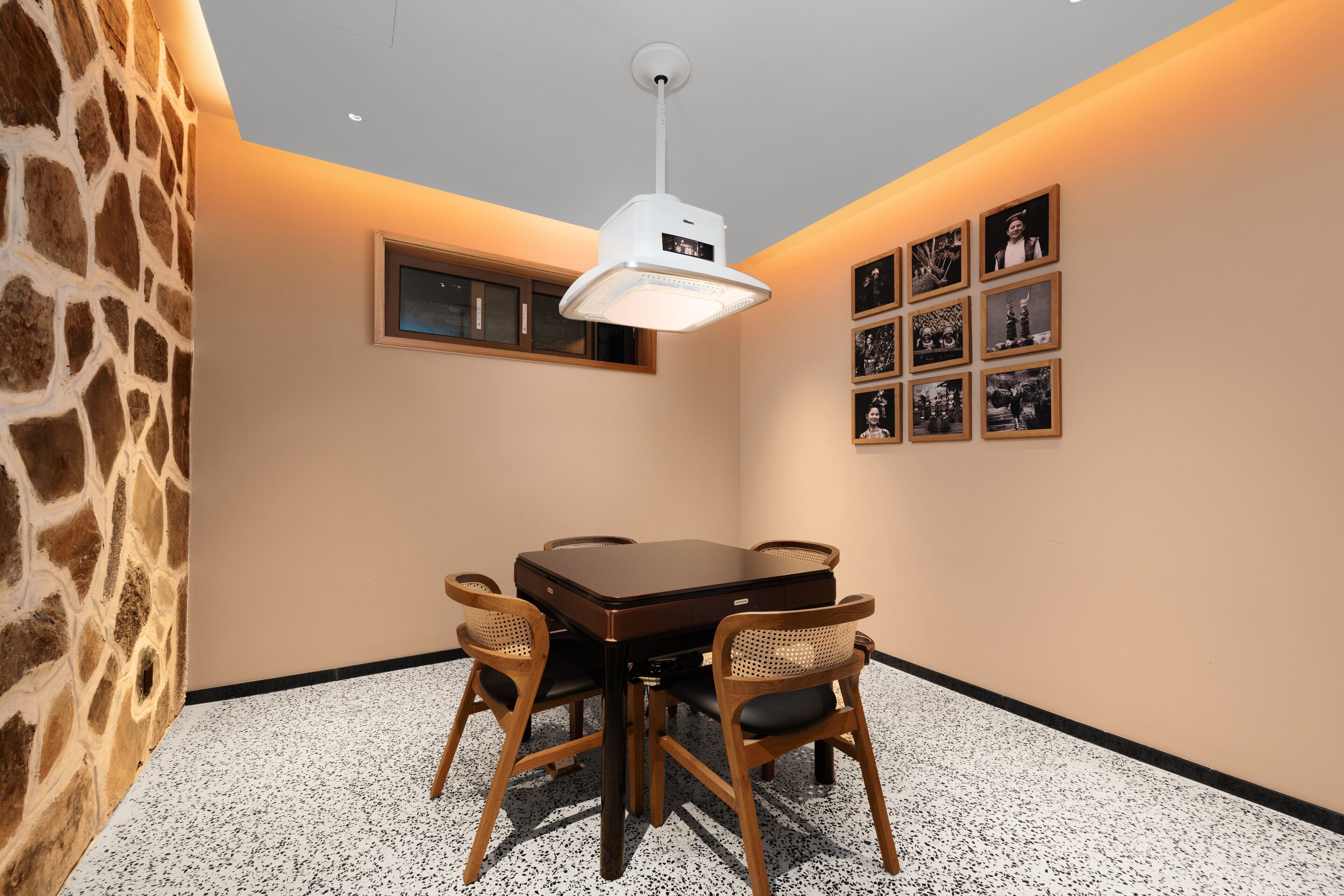 A conference room with a round table, four wooden chairs, a ceiling light, a window, and framed pictures on the wall.