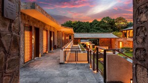 A stone building with a covered walkway and a view of trees in the background. - YAOJIA WATERFALL VILLAGE RESORT (Anshun)