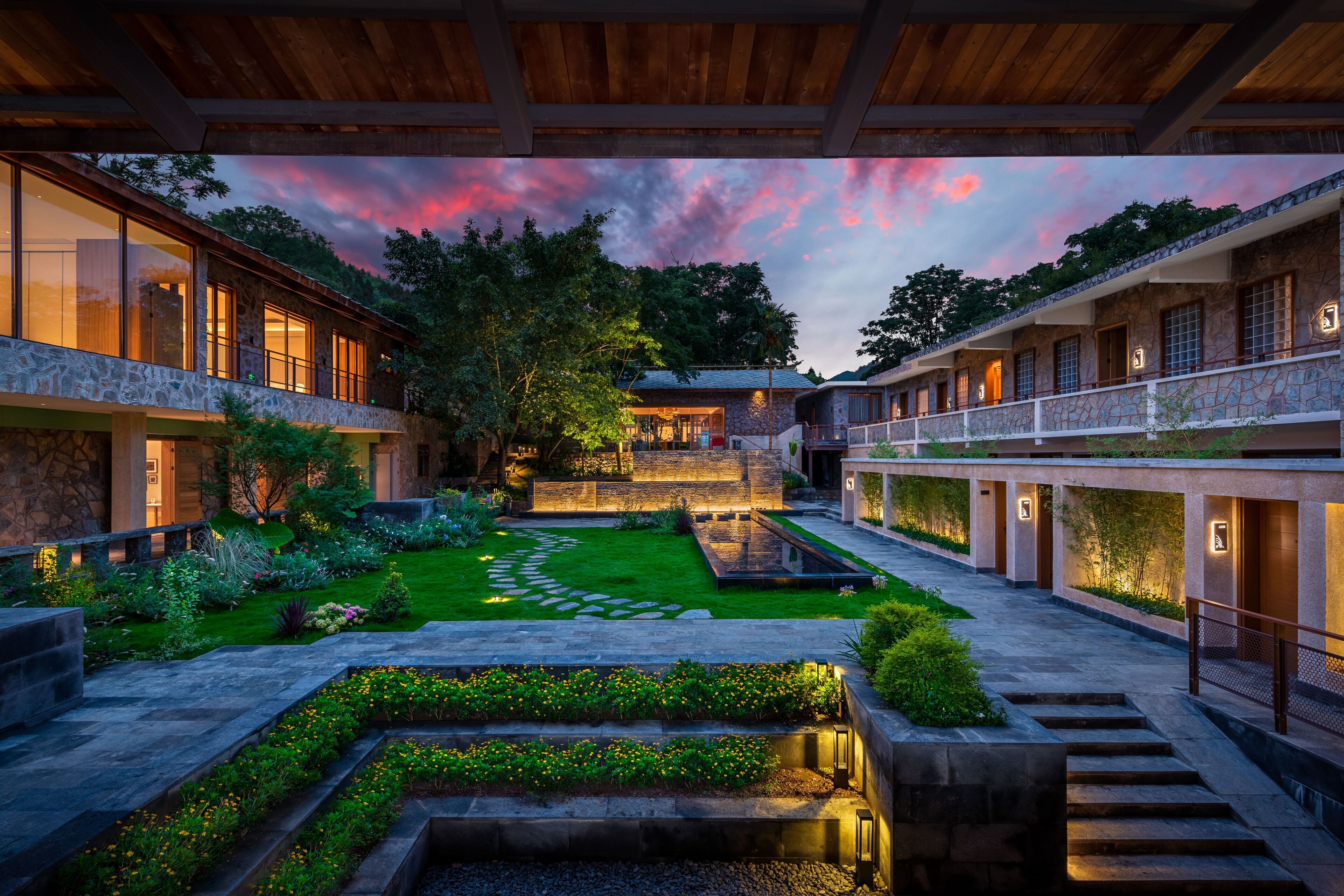 Un patio con senderos de piedra, un jardín central y una pérgola de madera.