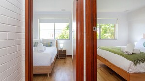 A hotel room with two beds, wooden flooring, a brick wall, and large windows with a view of greenery. - Modern Fremantle- Sunset Over the Ocean (Fremantle)