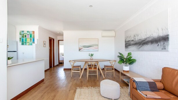 A modern living room with a wooden dining table, a sofa, and a large painting on the wall. - Modern Fremantle- Sunset Over the Ocean (Fremantle)