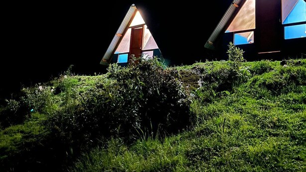 Two triangular-roofed structures with visible windows and doors, set on a grassy hill.